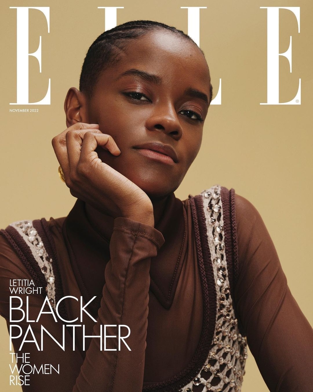 Close-up portrait of Letitia Wright on Elle Magazine cover, November 2023 issue, in sheer brown top and beaded dress, against tan background.