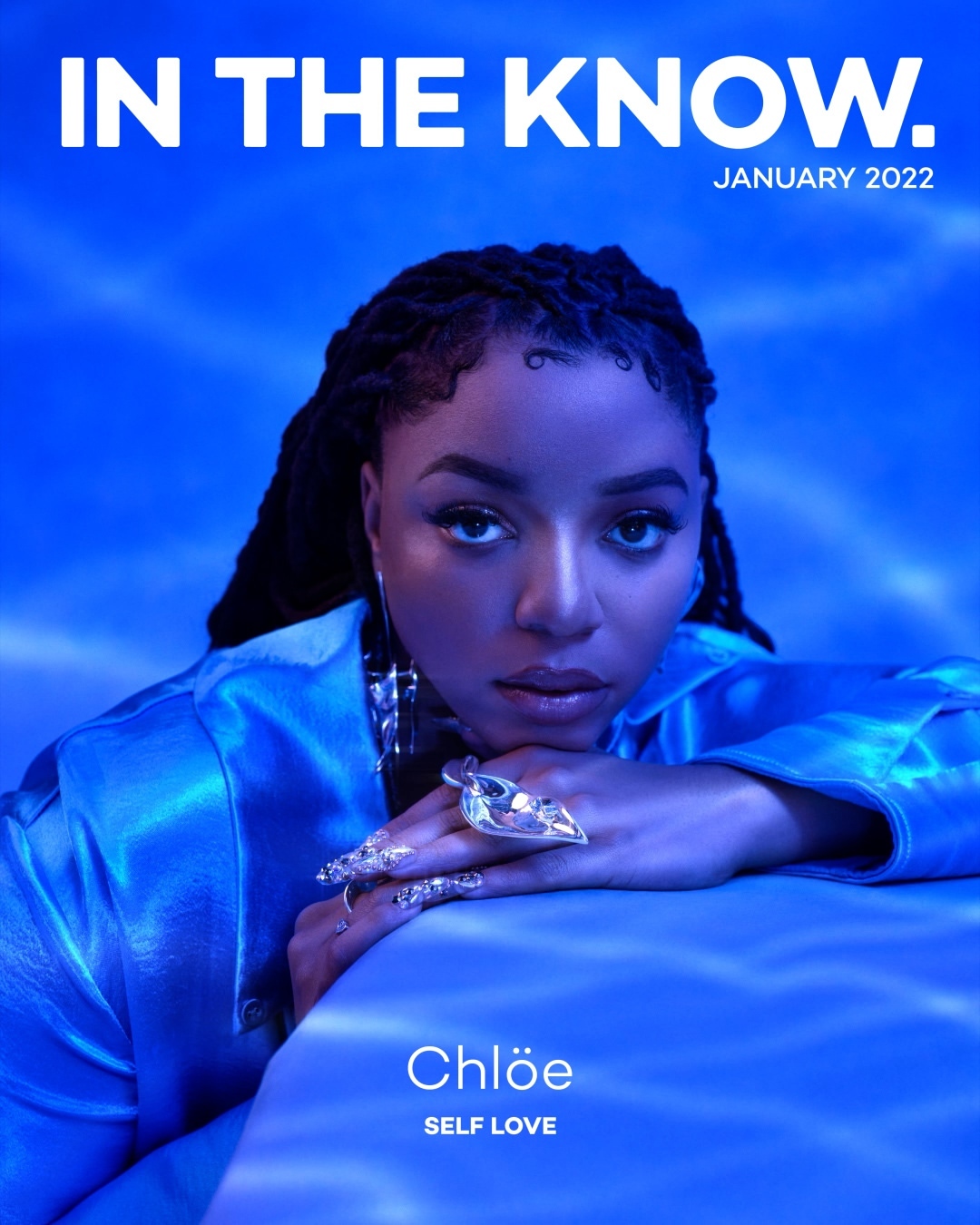 Close-up magazine cover featuring a woman with dark hair, wearing a blue satin top and large gemstone ring, against a blue background.