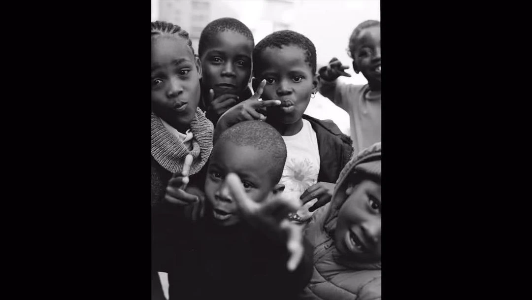 Black and white shot of a group of Black children in an outdoor setting, wearing casual clothing, captured with a close-up, eye-level angle.