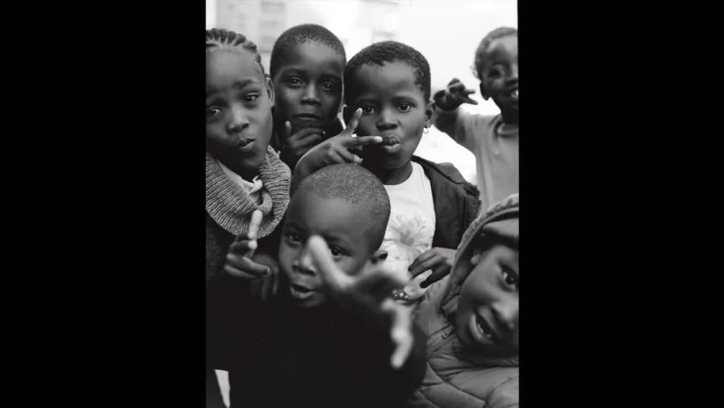 Black and white shot of a group of Black children in an outdoor setting, wearing casual clothing, captured with a close-up, eye-level angle.