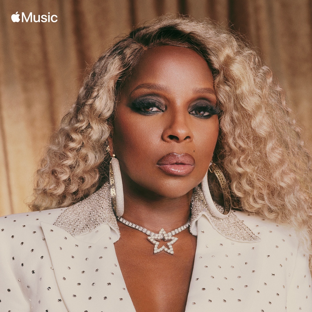 Close-up portrait of an African-American woman with blonde curly hair wearing a white blazer and jewelry against a neutral backdrop.