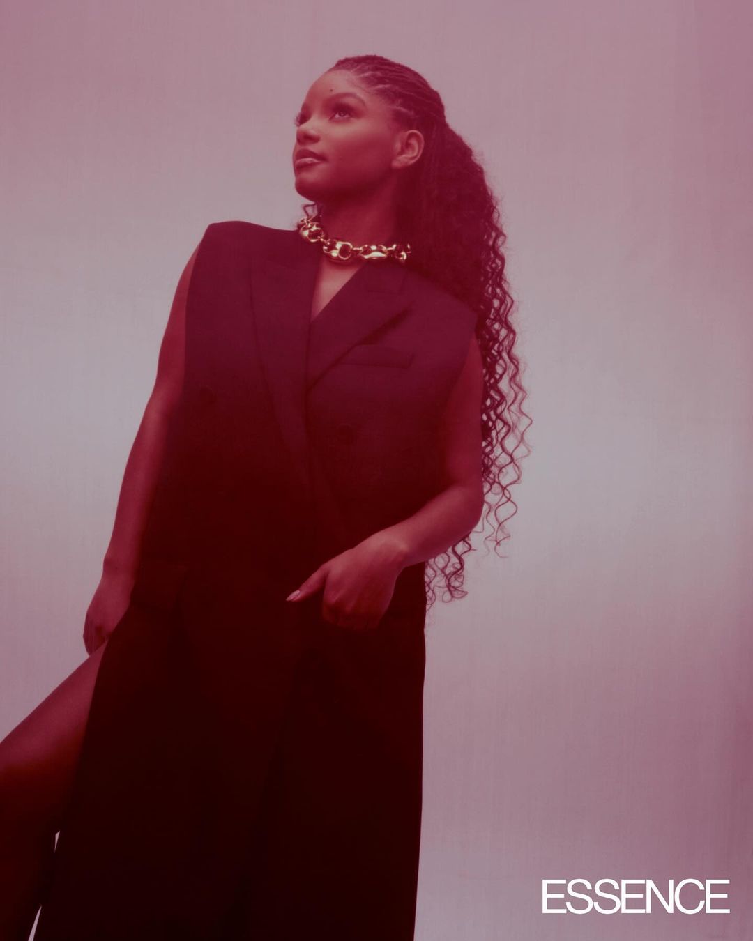 Glamorous portrait of a Black woman with long, curly hair wearing a black sleeveless dress and gold necklace against a light backdrop.