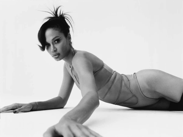 Model lying on a white seamless backdrop wearing a strappy swimsuit and winged eyeliner