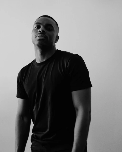 Black and white portrait of a Black adult male wearing a black t-shirt, looking directly at the camera against a plain background.