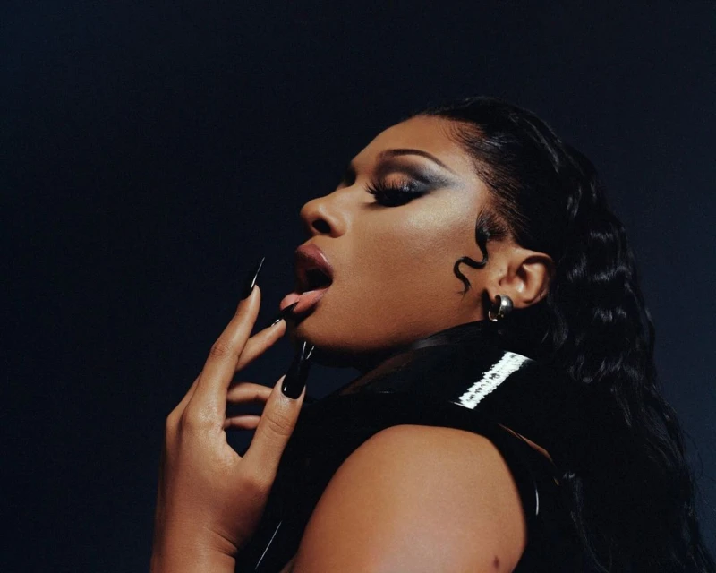 Glamorous portrait of a woman with long black hair, striking eye makeup, and long black nails, posing against a dark background.