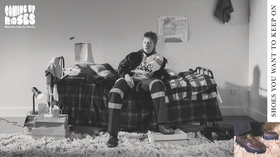 Indoor studio portrait of a model sitting on a bed covered in a plaid blanket, surrounded by shoe boxes and carpet, fashion and style.
