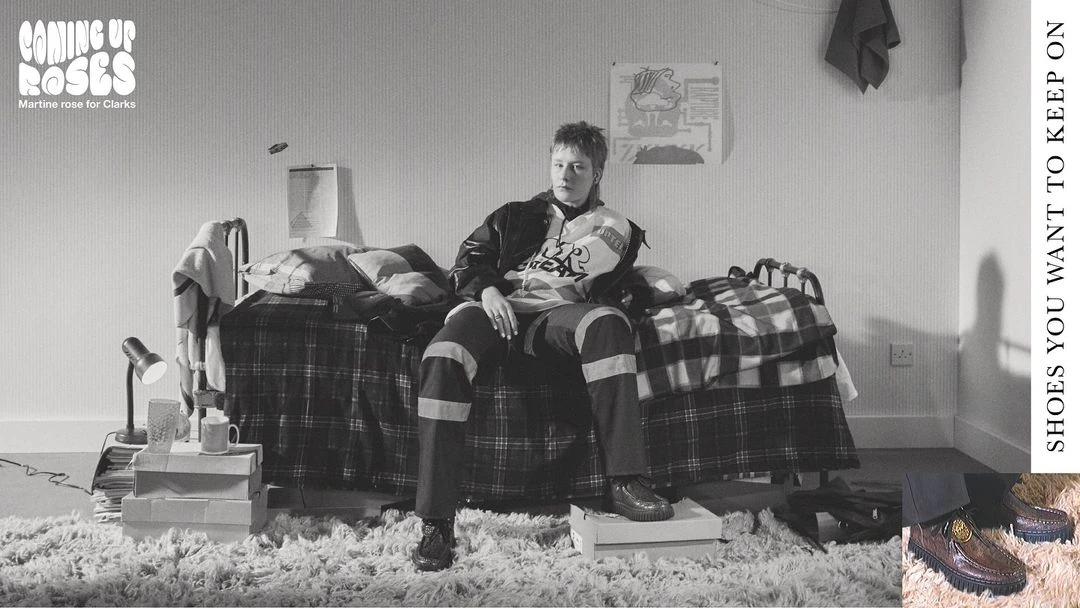 Indoor studio portrait of a model sitting on a bed covered in a plaid blanket, surrounded by shoe boxes and carpet, fashion and style.