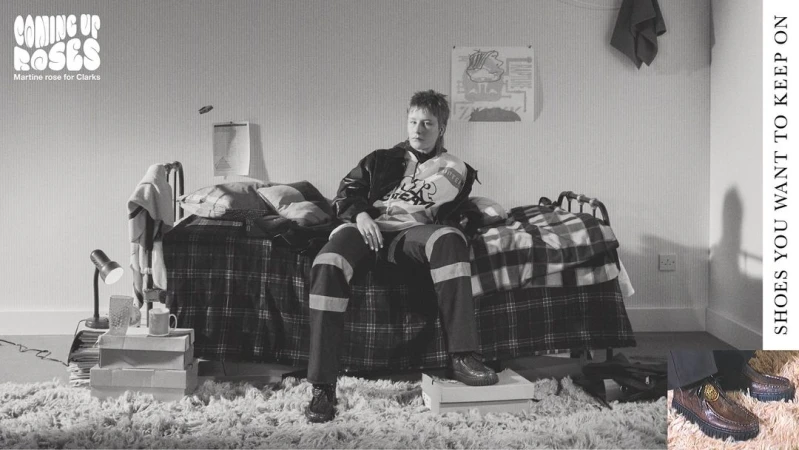 Indoor studio portrait of a model sitting on a bed covered in a plaid blanket, surrounded by shoe boxes and carpet, fashion and style.