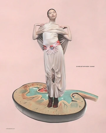 A woman poses in a beige dress on a kidney-shaped platform against a peach backdrop, showcasing fashion and artistic composition.