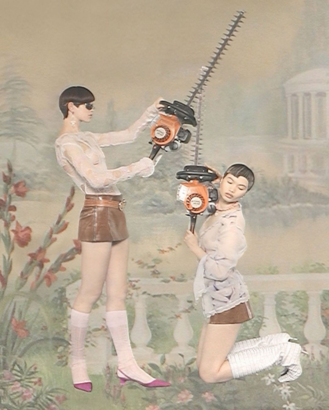 Two women in sheer tops and mini skirts hold hedge trimmers against a painted backdrop. Fashion editorial with garden machinery.