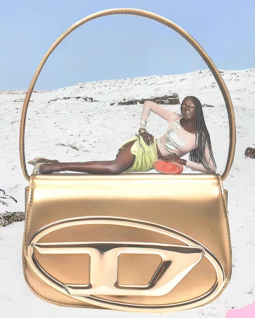 Model lying across a giant metallic gold handbag against a snowy landscape background