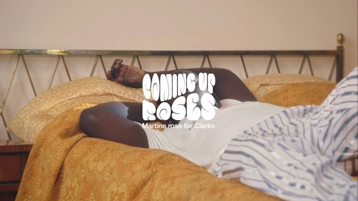 Adult laying on a bed in a bedroom with patterned bedding, wearing a white top, with text overlay for Martine Rose and Clarks.