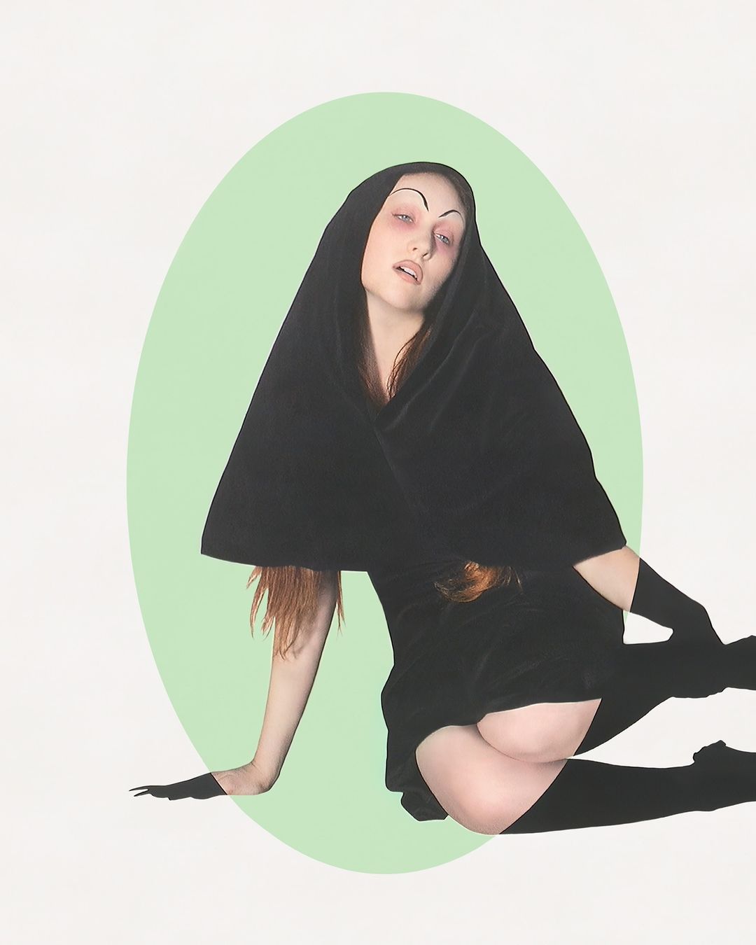 Woman in hooded black velvet dress, tights, and gloves posed against pastel green oval and white backdrop. Artistic fashion portrait.