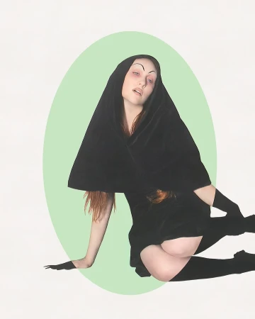 Woman in hooded black velvet dress, tights, and gloves posed against pastel green oval and white backdrop.  Artistic fashion portrait.