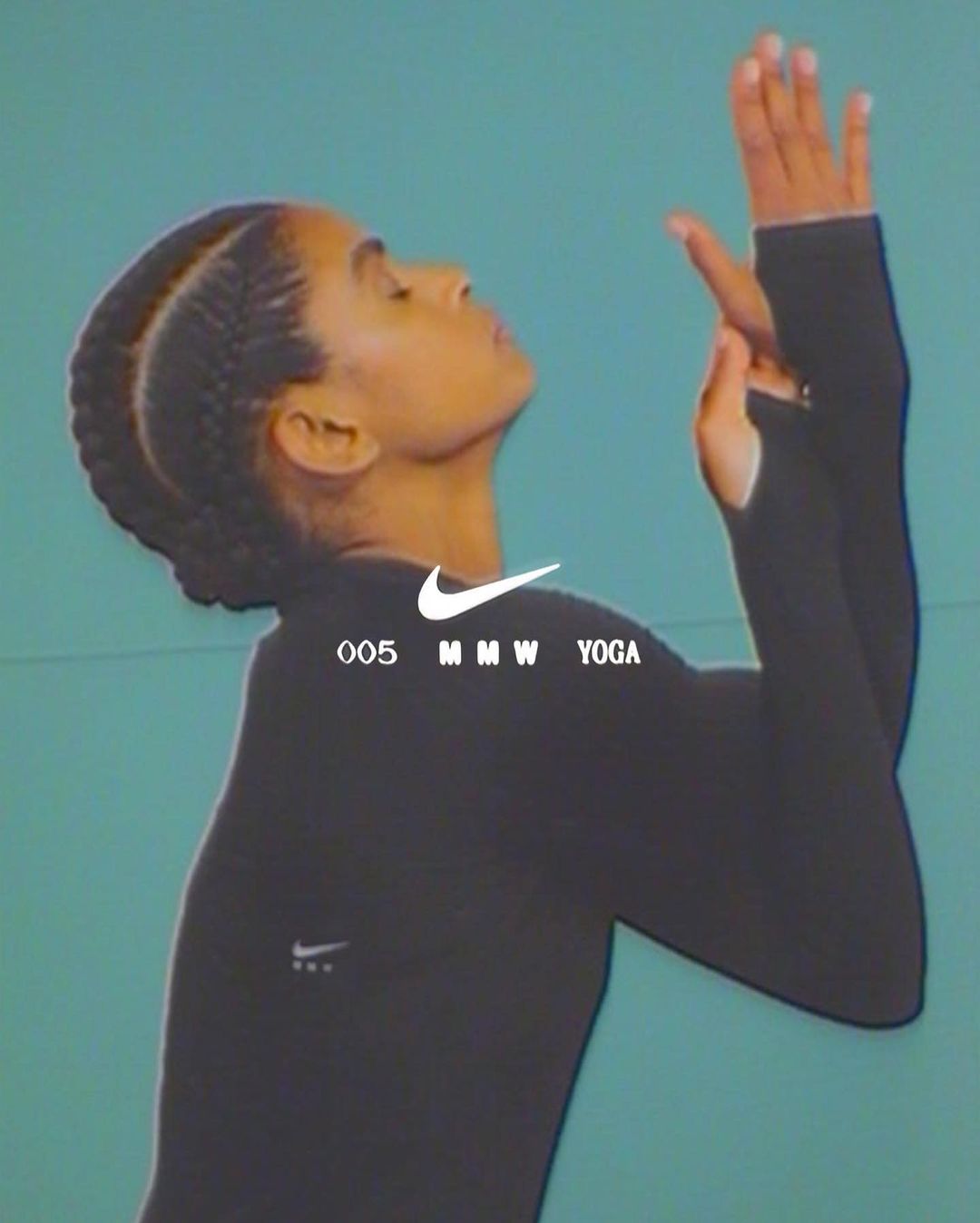 Side profile of an adult female in a black long-sleeved shirt with hands raised in a yoga pose, against a blue-green background.