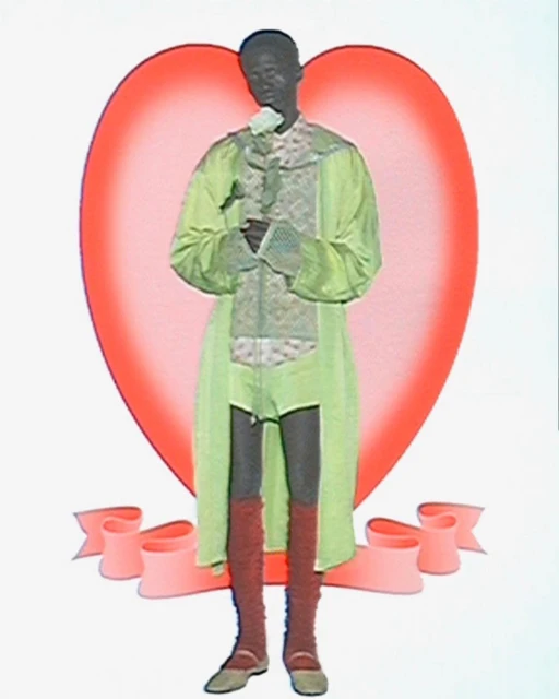 A person in costume holding a white rose, standing against a heart-shaped backdrop with a ribbon. The colors are light and soft.