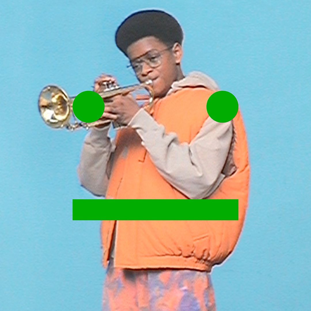 Teenage boy in orange vest playing a gold trumpet against a light blue background, wearing glasses and patterned pants.
