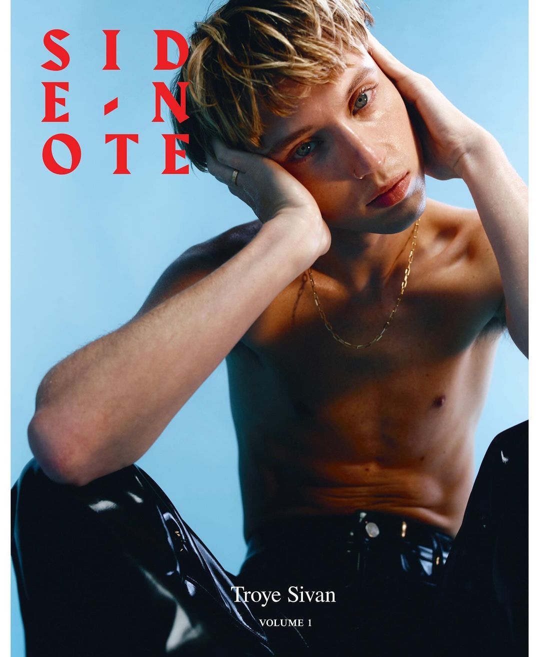 Troye Sivan poses shirtless in black pants with light blue background, album cover for 'Side Note,' blond hair, gold chain.