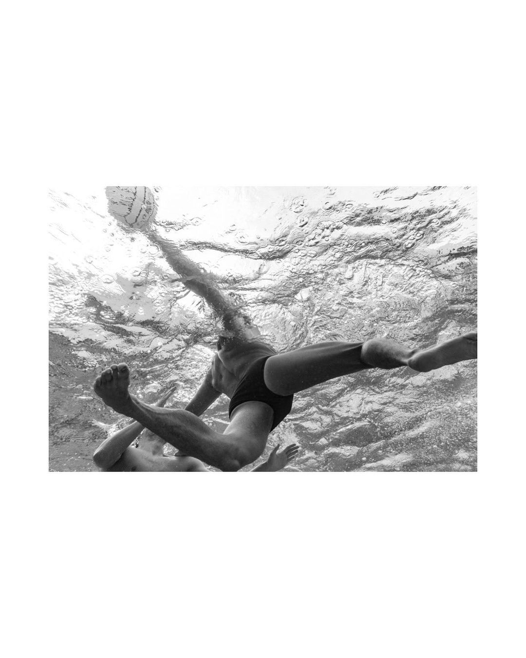 Underwater shot of two adult male water polo athletes competing for the ball, black and white photography, water background.