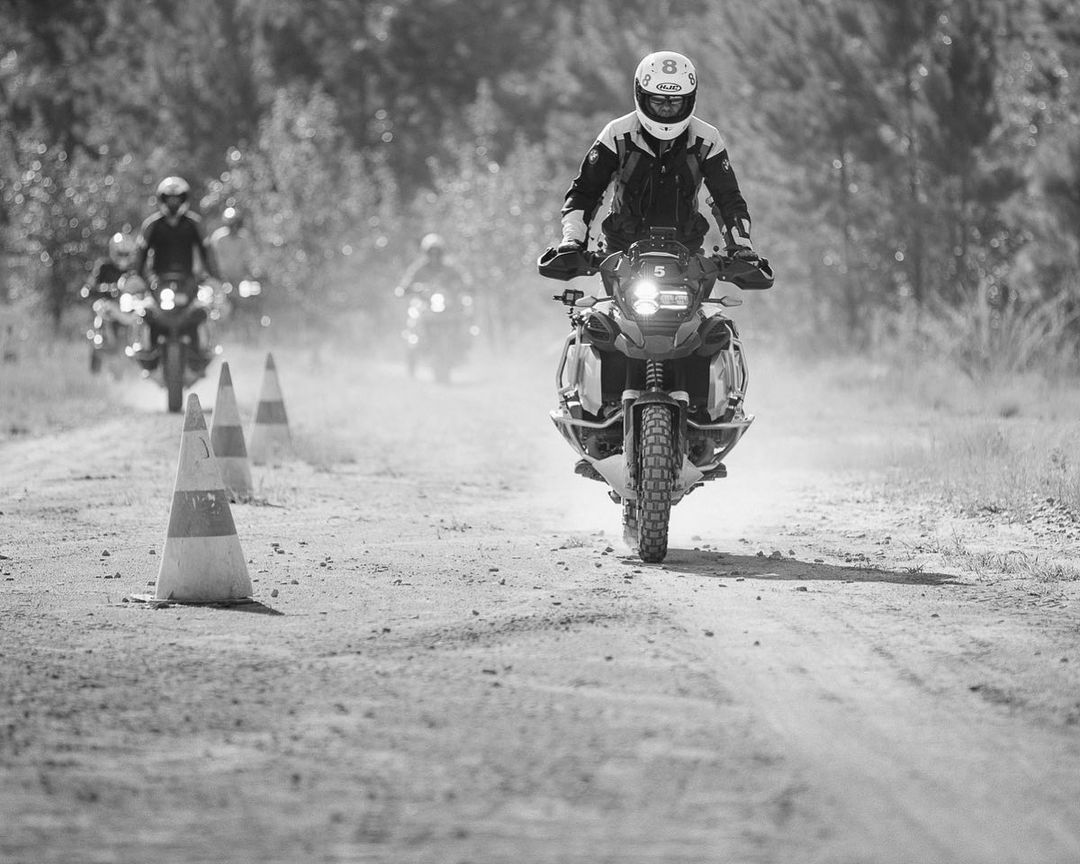 Monochrome shot of motorcycle riders navigating a dirt track, led by a rider in full gear, showcasing sport and outdoor adventure.