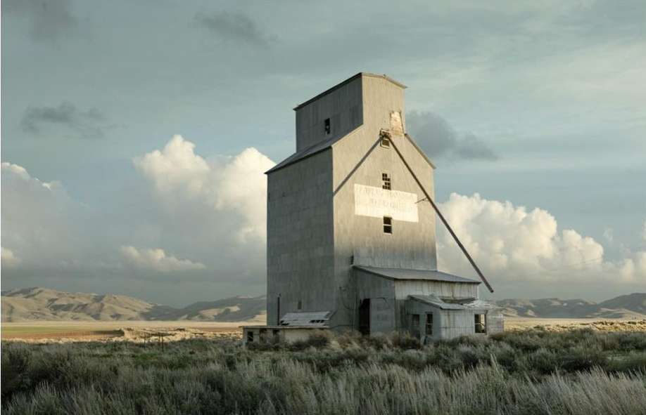 Grain elevator stands tall in a rural landscape under a sky filled with clouds, showcasing a blend of industrial and natural elements.