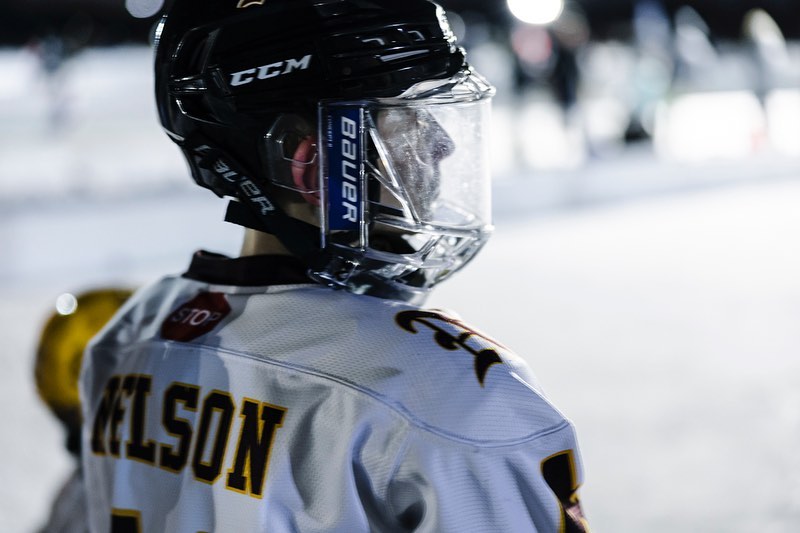 Hockey player in full protective gear and uniform, stands on the ice rink, captured at eye-level in a medium shot, wearing CCM helmet.