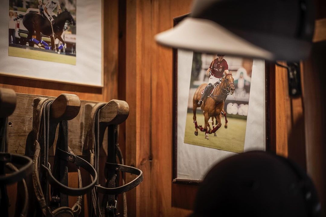 Photographs of polo players and horses adorn a rustic wooden wall, complemented by vintage riding gear and a sporting hat.