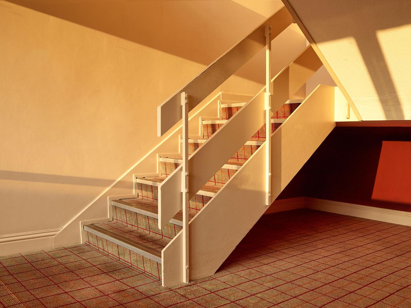 Interior view of a staircase with beige walls and carpeted steps in warm lighting, showcasing architectural design.