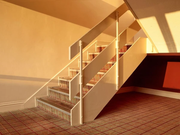 Interior view of a staircase with beige walls and carpeted steps in warm lighting, showcasing architectural design.