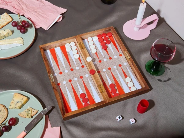 Overhead shot of an open backgammon board on a grey surface, surrounded by wine, cheese, crackers, a candle, and dice.