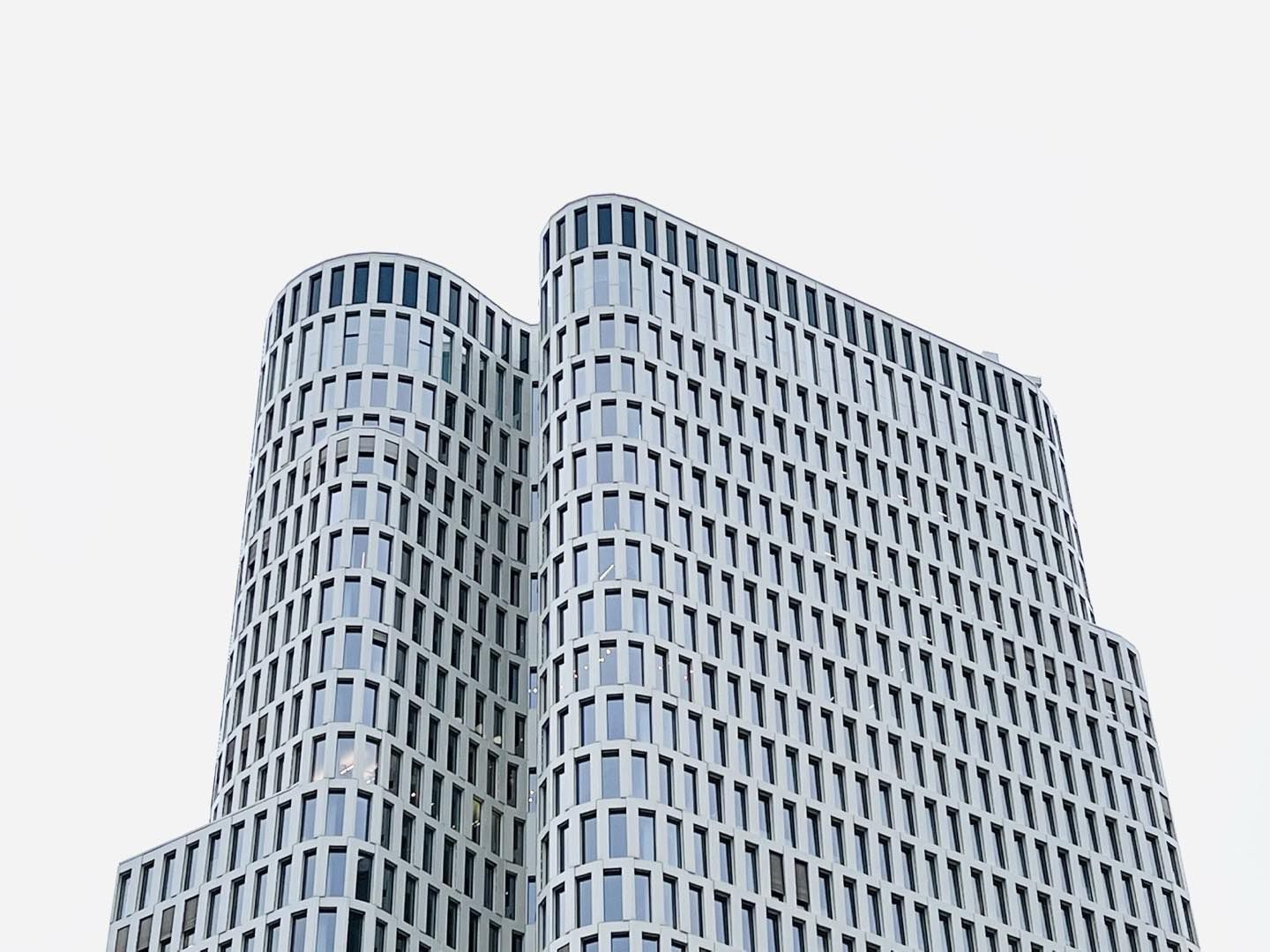 Exterior view of a modern, curved, high-rise building featuring many rectangular windows against a neutral background, showcasing architecture.