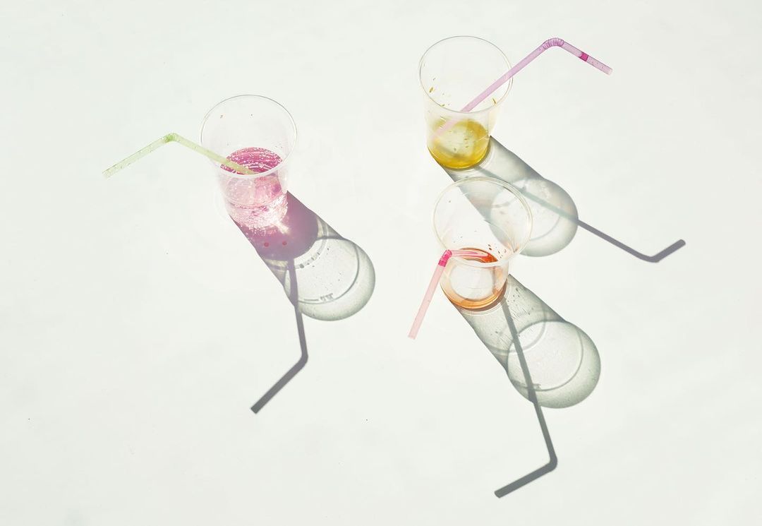Overhead shot of three plastic cups with colorful beverages and straws, casting shadows on a bright white surface.