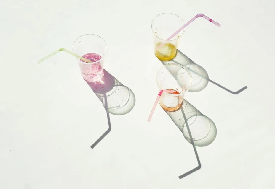 Overhead shot of three plastic cups with colorful beverages and straws, casting shadows on a bright white surface.
