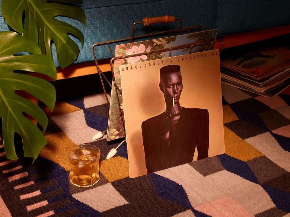 Grace Jones Nightclubbing album cover on patterned rug with drink and plant. Vintage record displayed indoors in a casual setting.