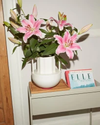 Pink and white lilies in a white ceramic vase resting on a grey console table with a magazine.