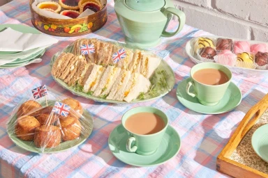 Afternoon tea spread with sandwiches, cakes, and tea cups on a plaid tablecloth photographed by Shaw & Shaw.