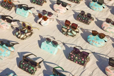 A flat lay arrangement of multiple sunglasses resting on patterned cases over a textured light background.