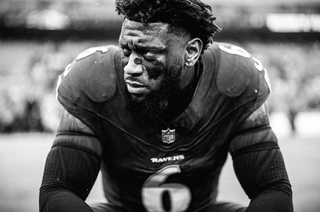 Black and white close-up of a male football player with eye black, wearing a jersey, and looking downward.
