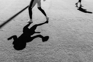 Monochrome low angle shot focusing on the legs and elongated shadows of two football players on a turf field