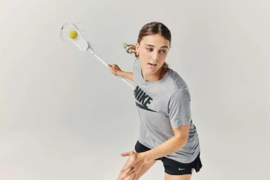 Female athlete holding a lacrosse stick with a yellow ball in the pocket against a white background