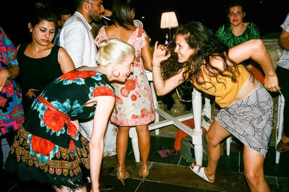 Candid shot of a diverse group of adults interacting at an indoor party, illuminated by lamp light and captured with a wide-angle lens.