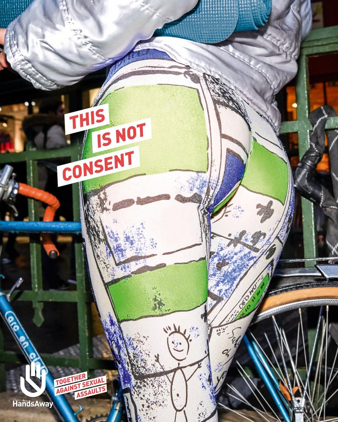 A woman stands with a bicycle wearing leggings with cartoon graphic and the words 'This is not consent' pasted over buttocks.