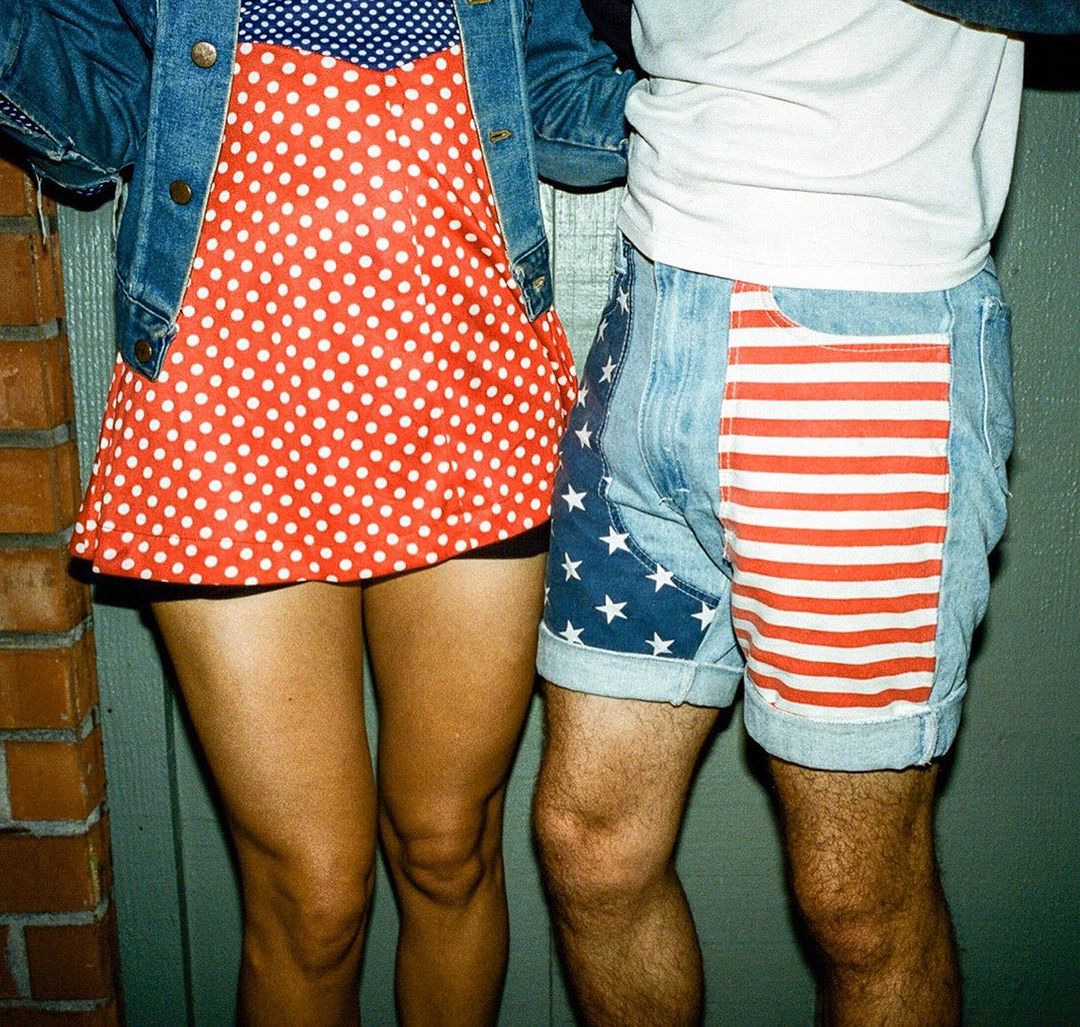 Two people in patriotic-themed clothing, one in a red polka dot top and denim jacket, the other in star and stripe denim shorts.