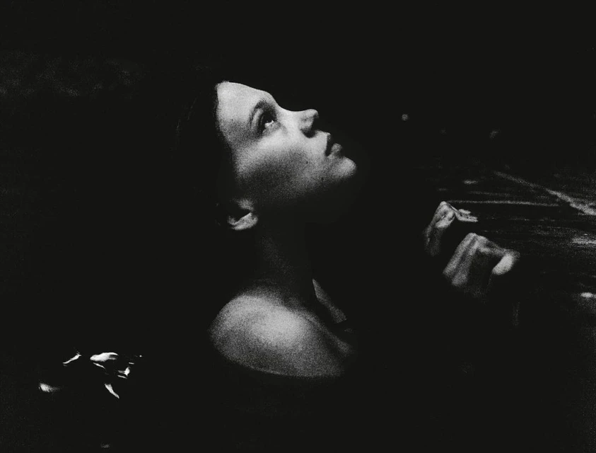 Monochromatic portrait of an adult woman looking up with an open expression. Dark, shallow focus with visible grain, and some visible water.