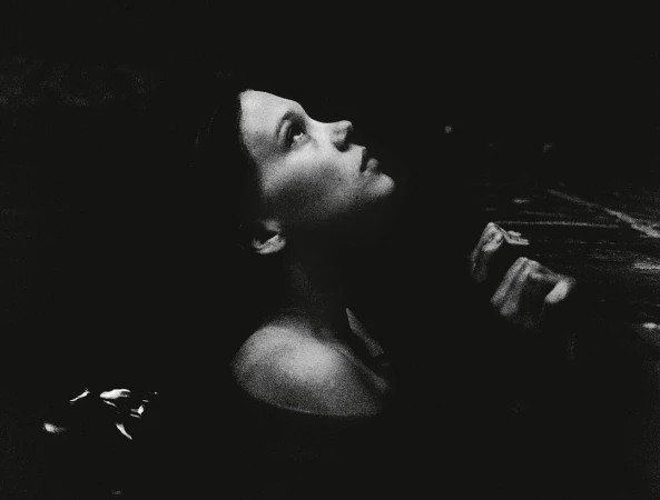 Monochromatic portrait of an adult woman looking up with an open expression. Dark, shallow focus with visible grain, and some visible water.