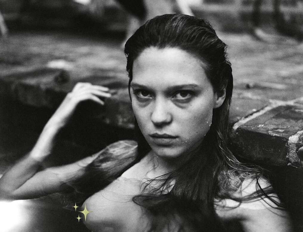 Black and white portrait of a woman in water, close up shot.  The woman has long dark hair and is partially submerged in the water.