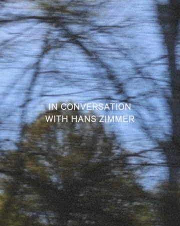 An abstract, slightly blurred image of bare tree branches against a soft blue sky, with the text overlay 'In Conversation With Hans Zimmer'.