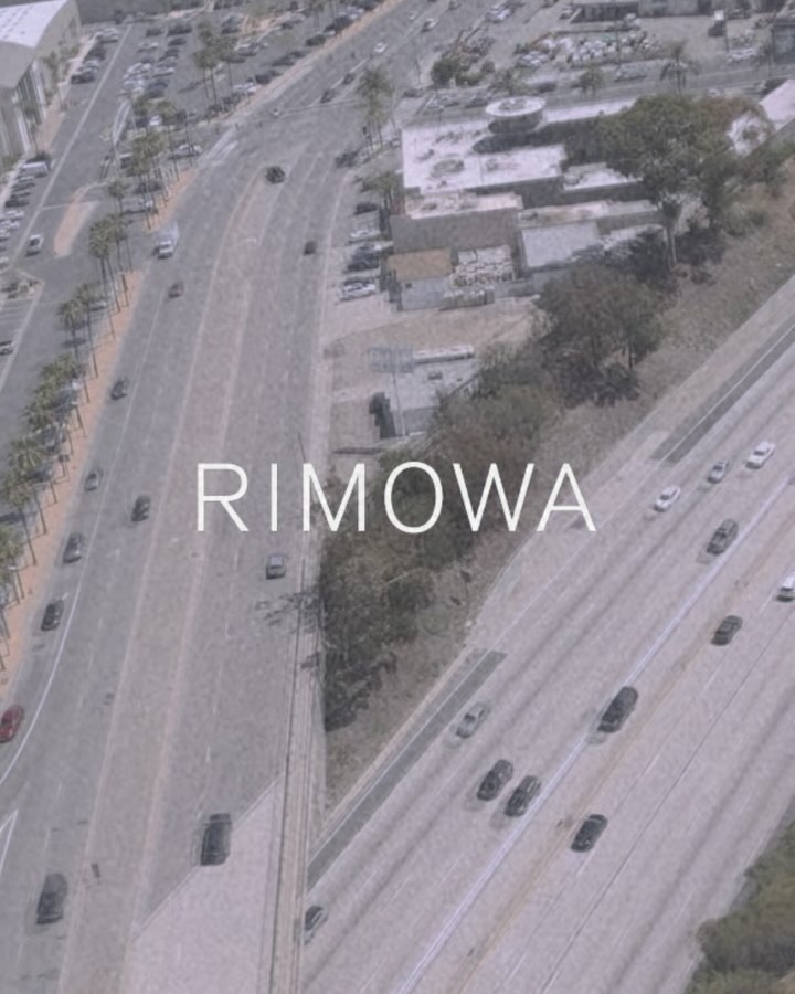 Aerial view of a multi-lane highway with cars and infrastructure during daytime, featuring the text "RIMOWA" overlaid on the image.