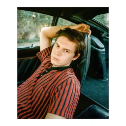 Portrait of Evan Peters seated inside a car wearing a red and black striped polo shirt by photographer Shelby Duncan