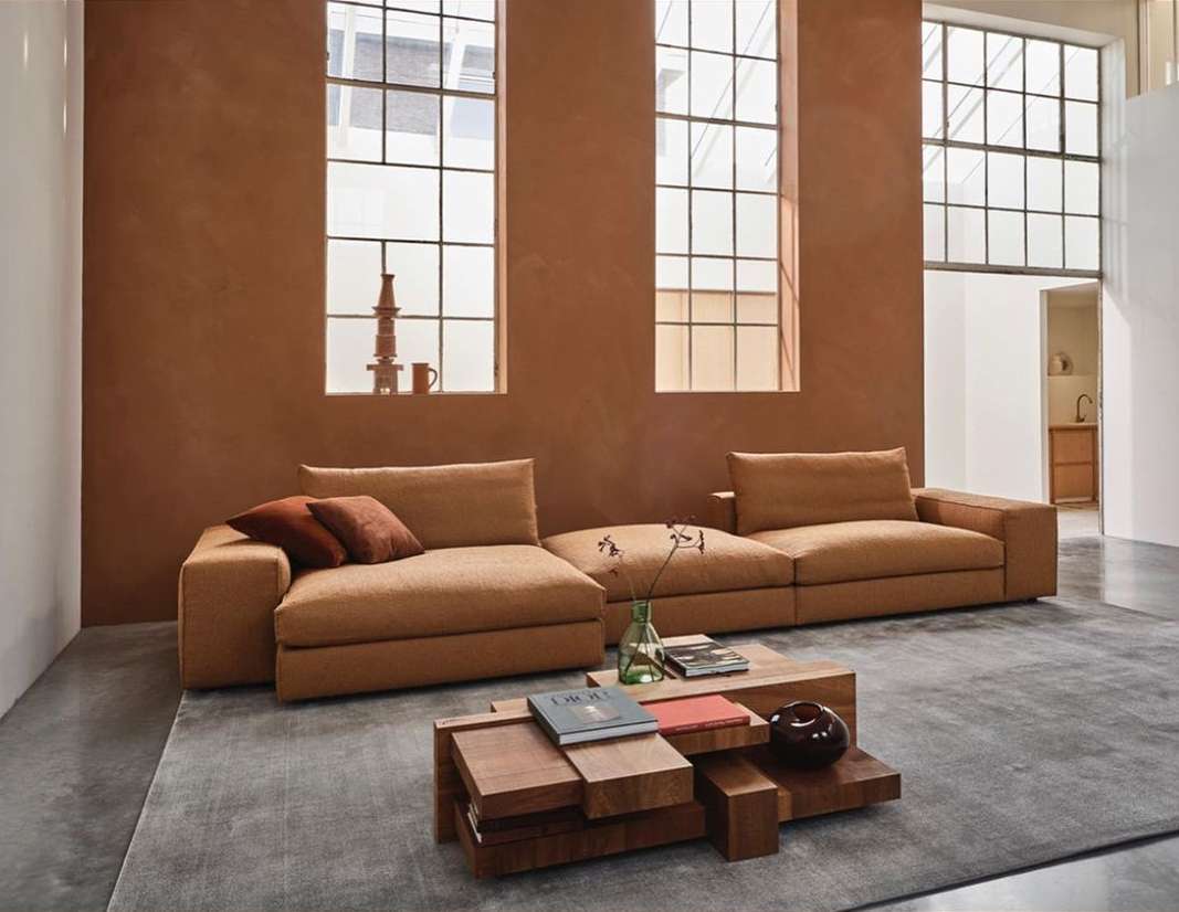 Living room interior with tan sofas, wooden coffee table with books, large windows, and tan wall paint, creating a cozy, modern space.